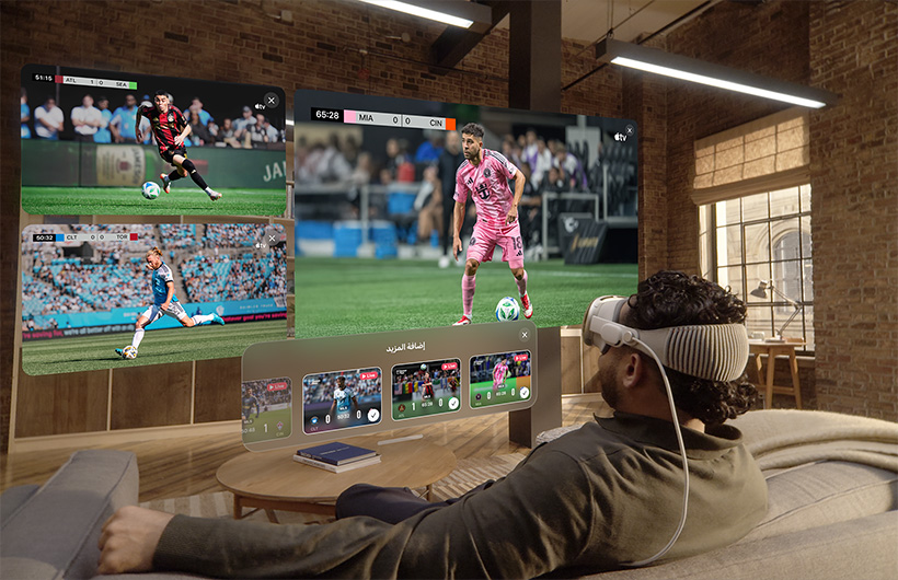 شخص يضع Apple Vision Pro على وجهه ويجلس على أريكة في غرفة الجلوس، وأمامه شاشة كبيرة إلى جانب شاشتين أصغر حجماً، وكل واحدة منها تعرض فعالية رياضية مختلفة. وفي أسفل الشاشة الكبيرة، تظهر نافذة اختيار كُتبت عليها عبارة إضافة المزيد
