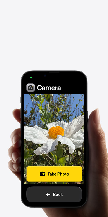 iPhone 16e screen showing simplified Camera app interface with a white flower in the frame, “Take Photo” button, and “Back button below