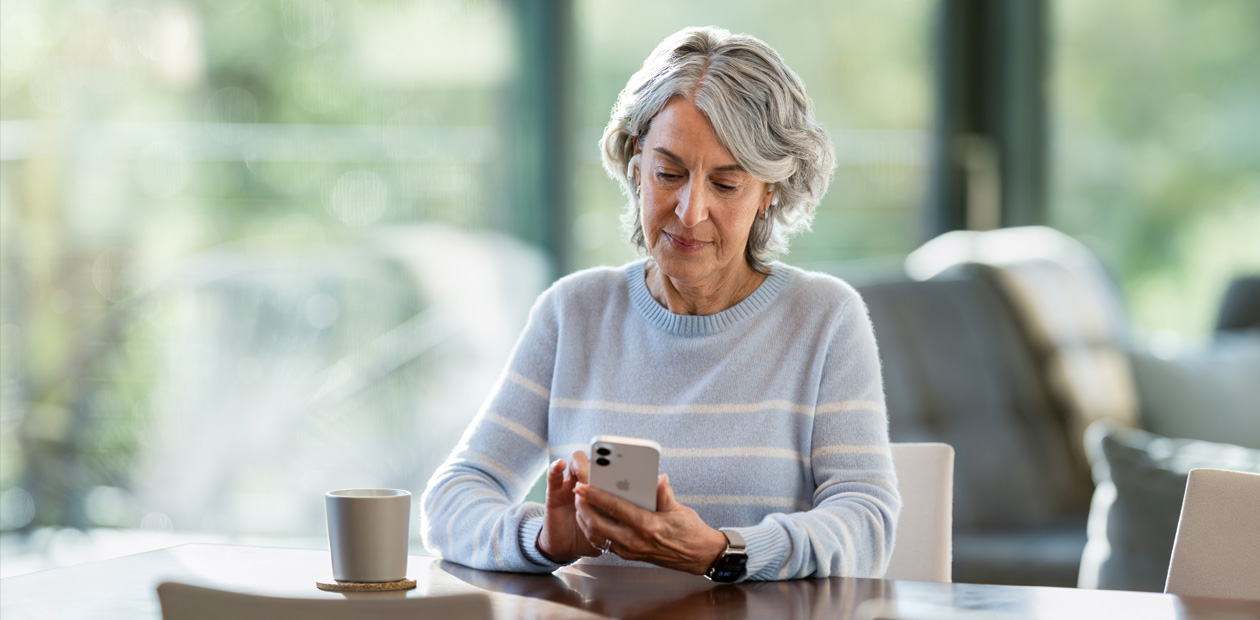 An elderly woman looking at an iPhone while sitting at a table.