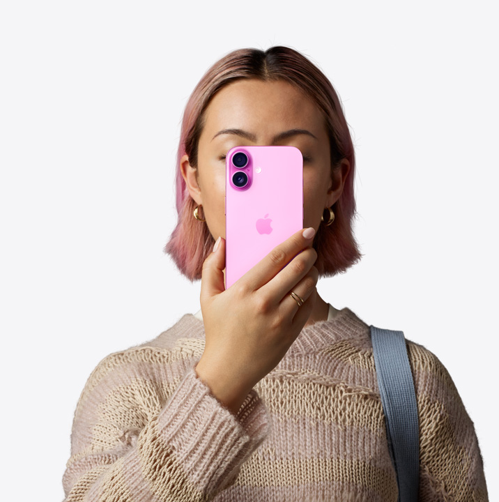 Eine Person hält ein iPhone 16 in Pink vor ihr Gesicht, sodass die Rückseite mit dem Zwei-Kamera-System links oben zu sehen ist.