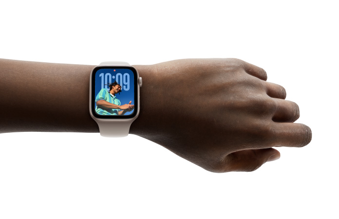 Close-up of Apple Watch in Rose Gold with rubber band on a person’s wrist, showing Time app in new Liquid Glass design