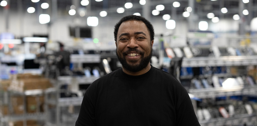 An employee stands in a logistics and repair center, smiling at the camera